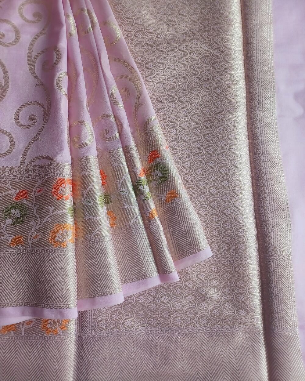 Georgette Saree in Lavender Shade with Silver zari weaves in the famous Banarasi Jaal work. Border has Banarasi floral motifs with Meena work.