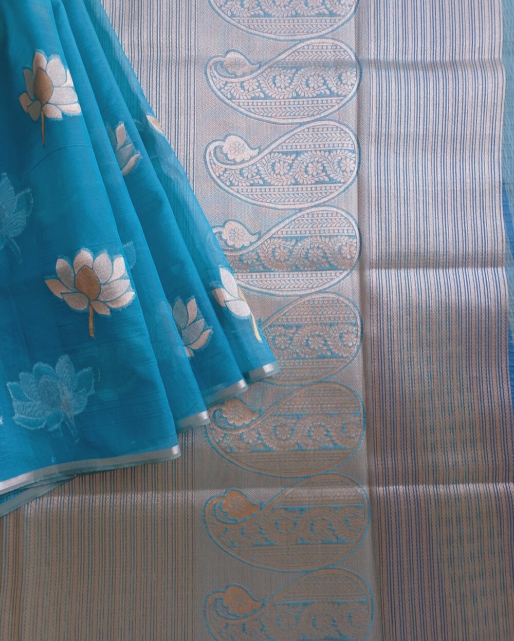 Organza saree in Light Blue shade with Lotus motifs woven all over saree in gold and silver combination. Has a simple thin border. Pallu has silver zari work.