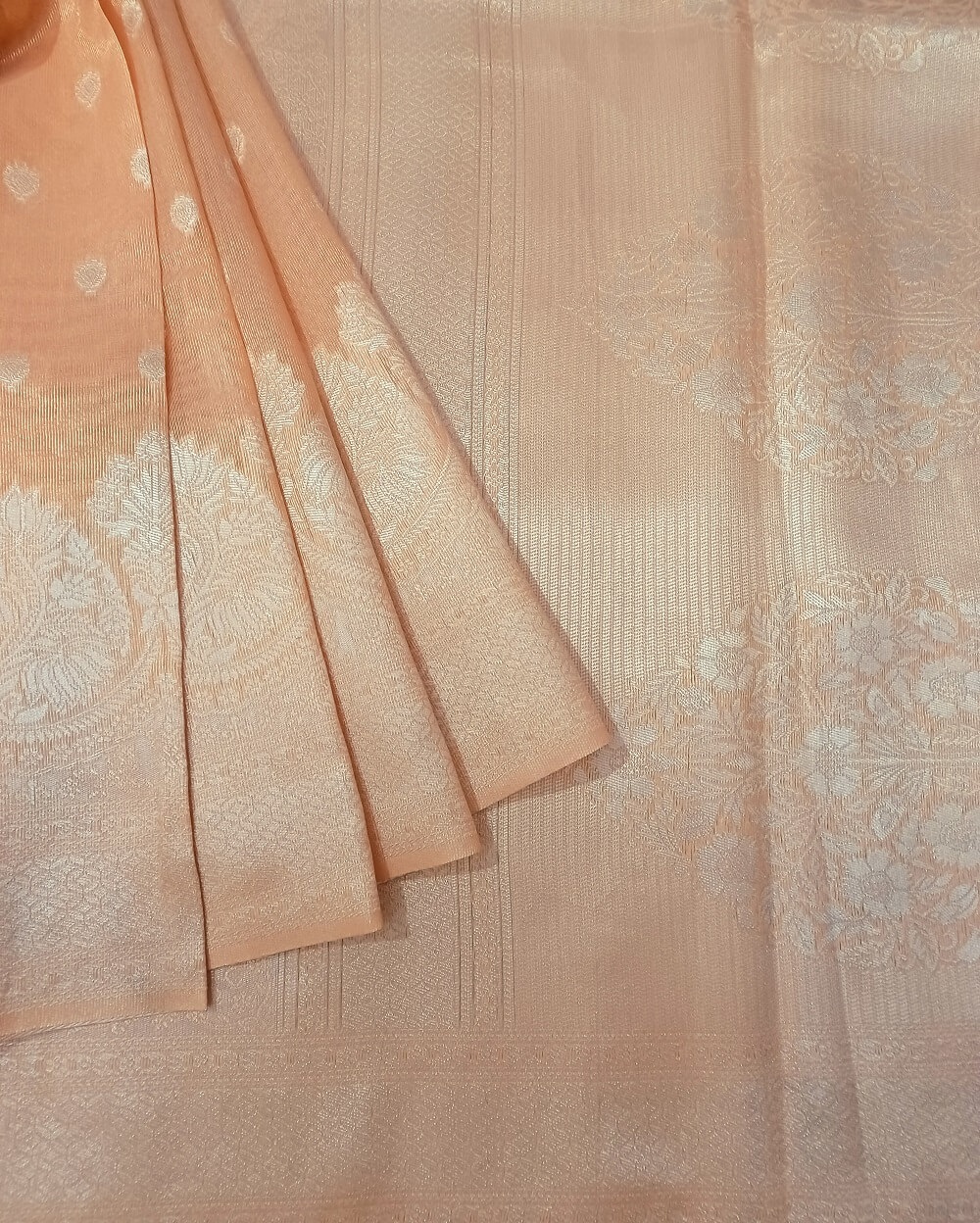 Tissue linen saree in Light Peach with Silver zari motifs woven in the pallu. Beautiful lotus flower patterns woven in the borders.