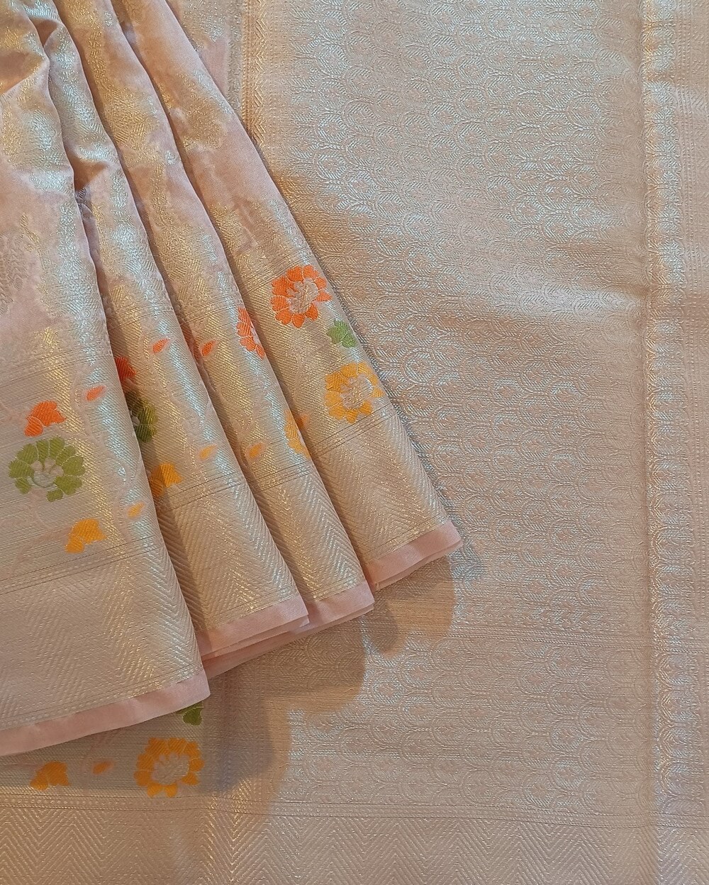 Georgette Saree in Light Rose Gold with Silver zari weaves in the famous Banarasi Jaal work. Border has Banarasi floral motifs with Meena work.
