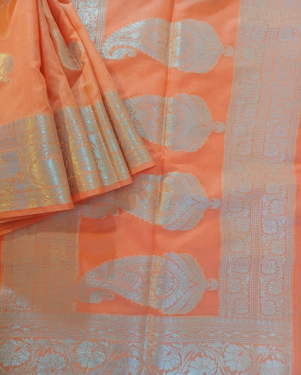 Georgette Saree in Peach shade with Silver zari weaves in the traditional leaf motifs. Border has Banarasi floral motifs. Pallu has Rich silver zari work.