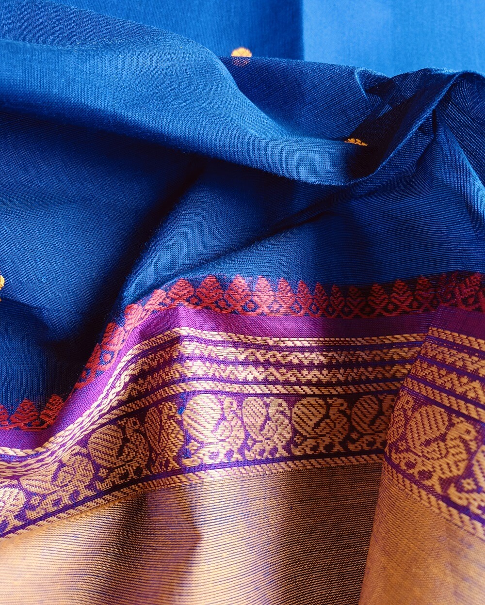 Handloom Kanchi Cotton Saree in Pleasant Shankhpushpi flower Blue with Purple border, it has Buttas on Saree and Thread Border with traditional Peacock and Mango Motifs.