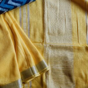 Lemon Yellow linen saree with silver border comes with an extra indigo color hand block printed mul mul cotton blouse piece. The saree comes with a plain body in very soothing shade with a subtle silver zari border. The pallu is simple with silver stripes. The blouse piece is running blouse piece that comes along with saree and the additional one is a beautiful Indigo hand block printed.