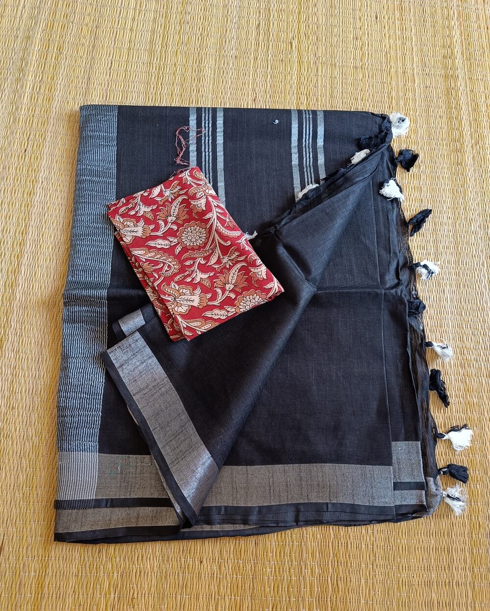Black linen saree with silver tissue zari border and contrast handcrafted - hand block printed mul mul cotton blouse piece, The Linen saree comes with a plain body in very soothing shade with a subtle silver tissue zari border. The pallu is simple with silver stripes. The blouse piece is running blouse piece that comes along with saree and the additional one is a beautiful hand block printed.