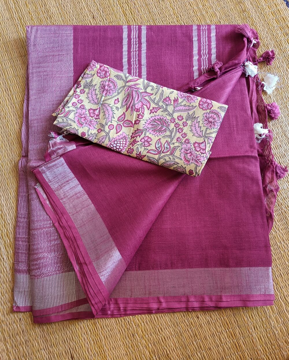 Dark Pink linen saree with silver tissue zari border and a light yellow handcrafted - hand block printed mul mul cotton blouse piece, The Linen saree comes comes with a plain body in very soothing shade with a subtle silver tissue zari border. The pallu is simple with silver stripes. The blouse piece is running blouse piece that comes along with saree and the additional one is a beautiful hand block printed