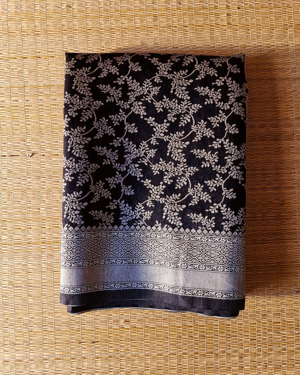Banarasi Cotton Saree in Black colour with Cream resham threads woven all over. It has traditional Banarasi floral motifs in jaal weaves which is a very famous traditional weave where the motifs are interconnected throughout the saree.