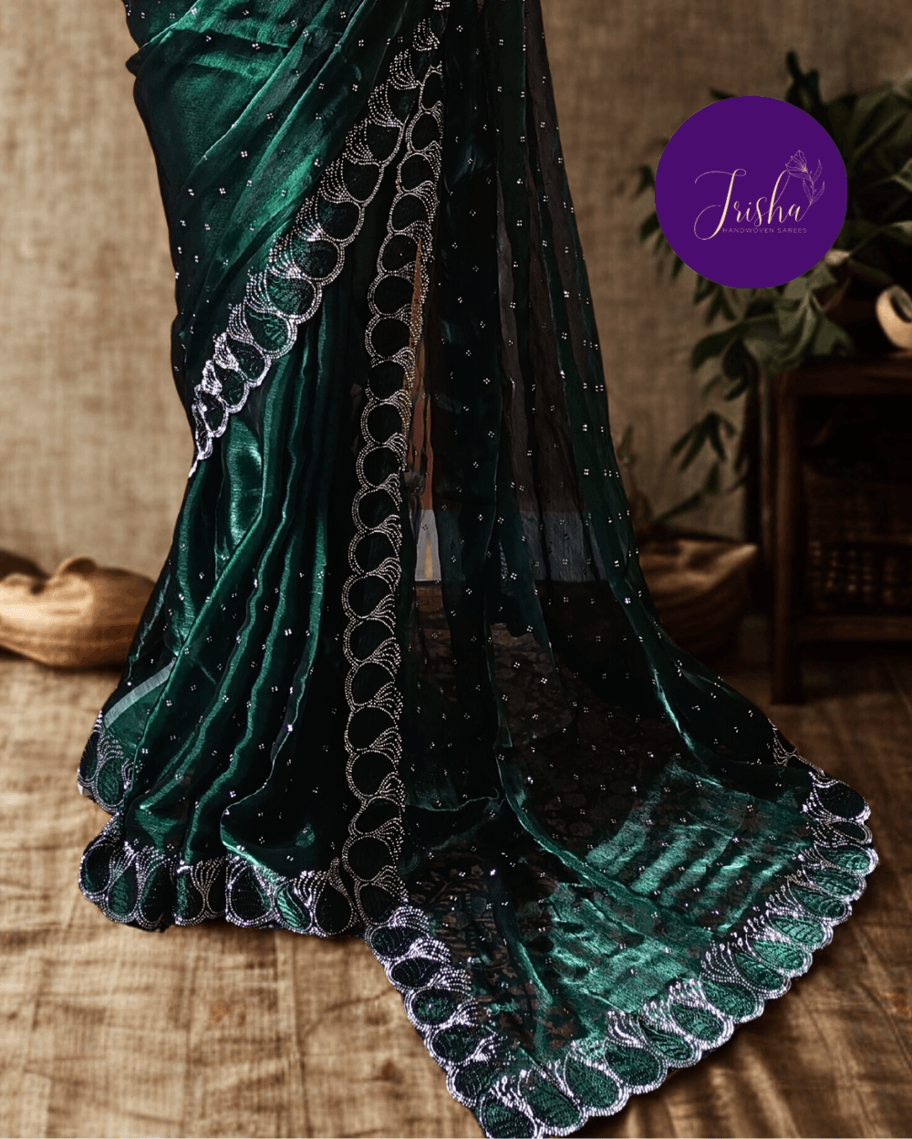 Jimmy Choo Organza silk saree in Emerald Green shade with black and white Swarovski crystal work in the border. The saree has Swarovski work on the shoulder part and the skirt portion of the saree in the form of small buttas. The Pallu is beautifully done in a C shape work pattern.
