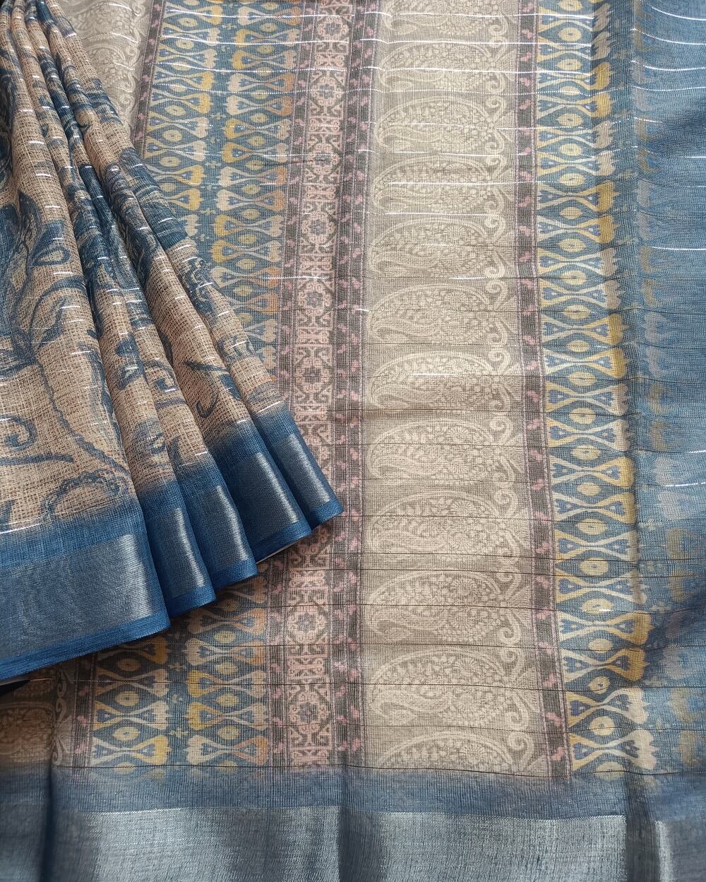 Jute Blue shade Semi Linen saree with silver tissue zari border, this saree comes with digital prints all over with a subtle silver tissue zari border. The pallu is simple with prints.