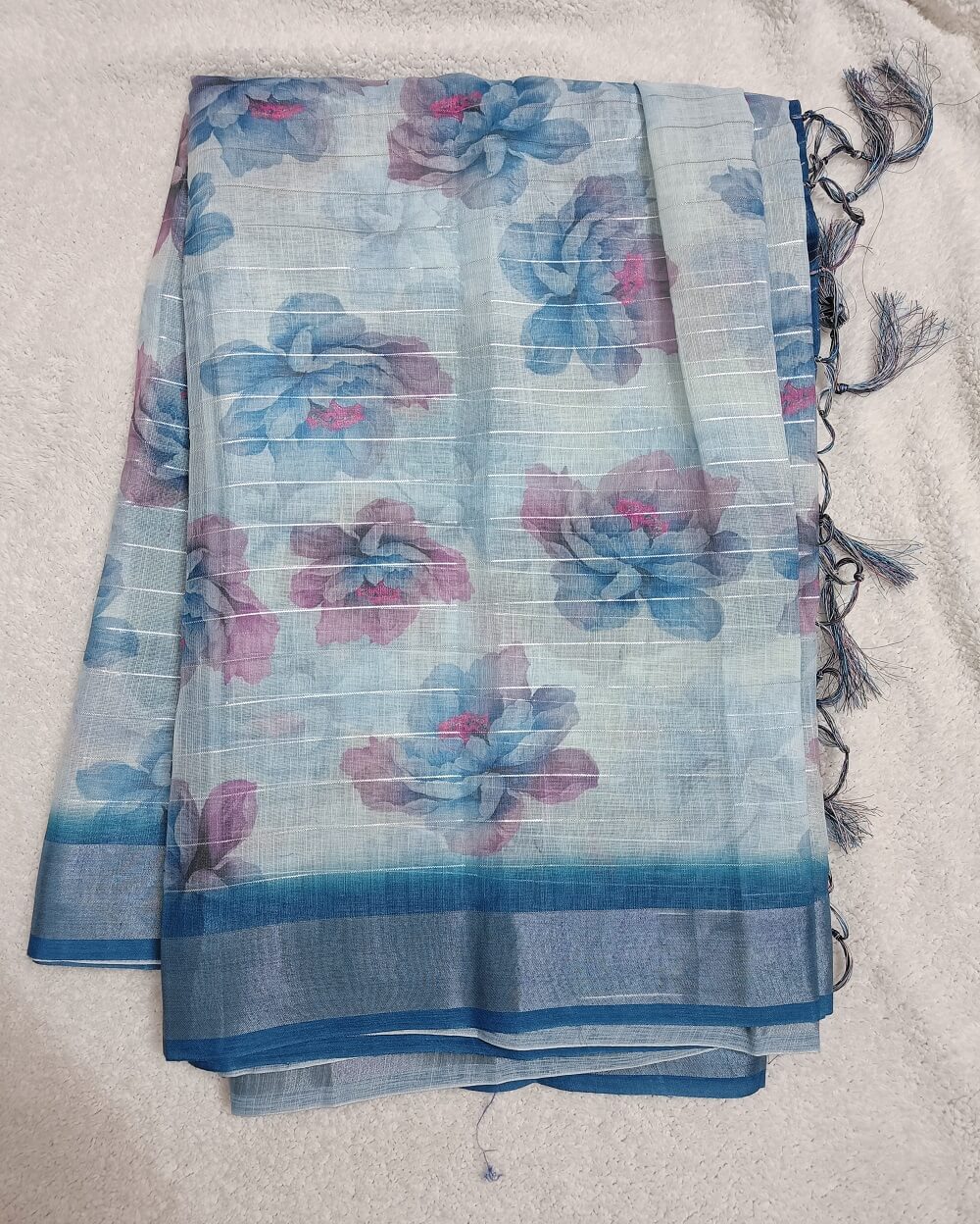 Sky Blue shade Semi Linen saree with silver tissue zari border, this saree comes with digital prints all over with a subtle silver tissue zari border. The pallu is simple with prints.
