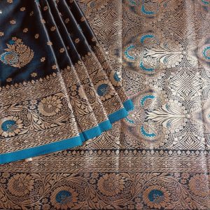 Banarasi Satin silk saree in Dark Indigo Blue shade dual tone with floral motifs in light gold zari weaves all over the body. Very unique meenakari work done on the motifs in the base fabric shade. It has a self border with gold work floral motifs. The Pallu is richly woven with intricate Banarasi floral motifs. Meenakari work has been done In the border and pallu that compliments the whole look of the saree. It includes self embossed blouse piece with gold border in same design as the saree.