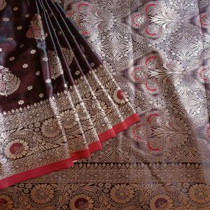 Banarasi Satin silk saree in Dark Brownish Maroon shade dual tone with floral motifs in light gold zari weaves all over the body. Very unique meenakari work done on the motifs in the base fabric shade. It has a self border with gold work floral motifs. The Pallu is richly woven with intricate Banarasi floral motifs. Meenakari work has been done In the border and pallu that compliments the whole look of the saree. It includes self embossed blouse piece with gold border in same design as the saree.