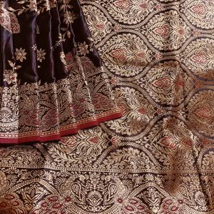 Banarasi Satin silk saree in Dark Brownish Maroon shade dual tone with peacock and creeper motifs in light gold zari weaves all over the body. Very unique meenakari work done on the motifs in the base fabric shade. It has been woven in the most famous jaal weaves i.e. All the motifs are connected throughout the saree. It has a self border with gold work floral and peacock motifs. The Pallu is richly woven with intricate Banarasi floral motifs. Meenakari work has been done In the border and pallu that compliments the whole look of the saree. It includes self embossed blouse piece with gold border in same design as the saree.