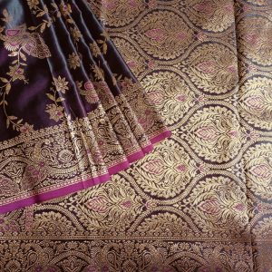 Banarasi Satin silk saree in Dark Wine Purple shade dual tone with peacock and creeper motifs in light gold zari weaves all over the body. Very unique meenakari work done on the motifs in the base fabric shade. It has been woven in the most famous jaal weaves i.e. All the motifs are connected throughout the saree. It has a self border with gold work floral and peacock motifs. The Pallu is richly woven with intricate Banarasi floral motifs. Meenakari work has been done In the border and pallu that compliments the whole look of the saree. It includes self embossed blouse piece with gold border in same design as the saree.